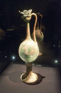 The Belitung Ewer stands over a metre tall. Incised around the body is a lozenge motif with leafy fronds, the same West Asian design shown on the green-splashed and blue-and-white dishes displayed nearby. The form is also seen in white ware, but was clearly modelled on metalwork: a similar ewer with a long handle and dragon-head stopper - but older and smaller and in gilded bronze - was preserved at the Horyu-ji Buddhist temple in Nara, Japan.